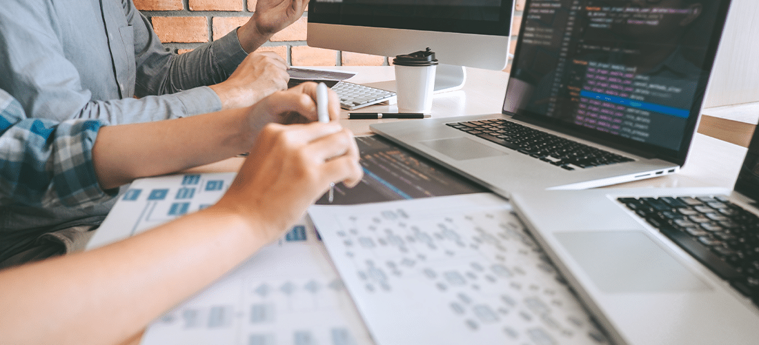 Web designers looking at laptop screen and paper mock-ups.