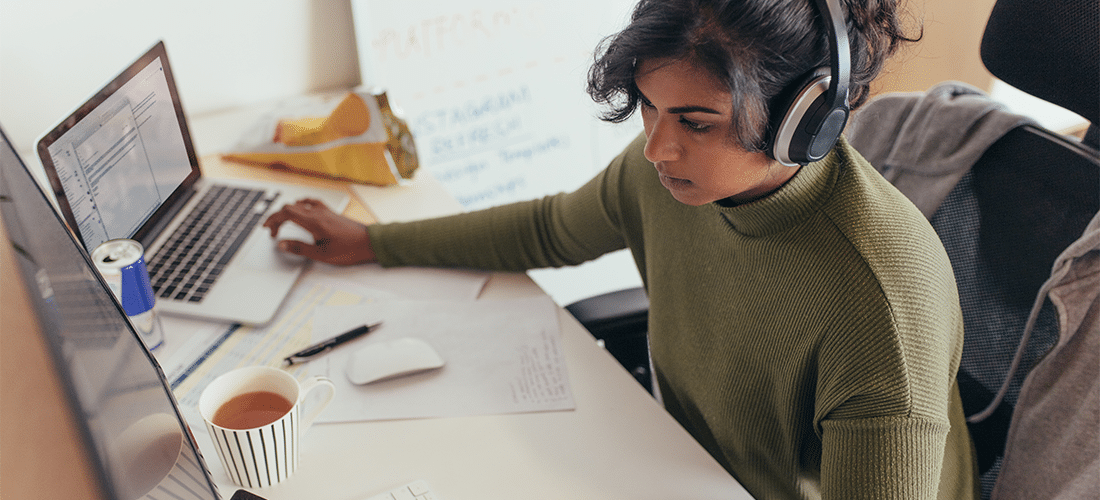 Programmer coding on a desktop computer and laptop at her desk in office.