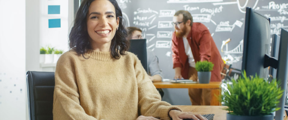 Woman Videographer Works on Her Personal Computer, Smiles on Camera.