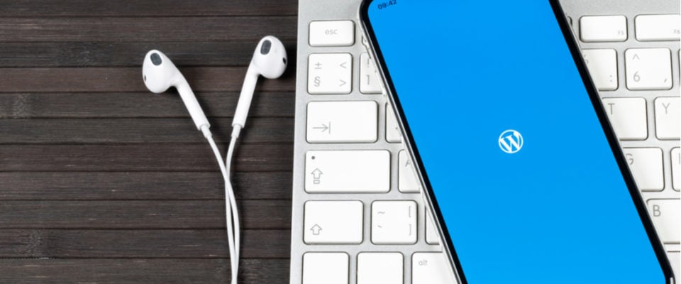 Picture of an Apple keyboard with headphone and a phone with WordPress logo pulled up