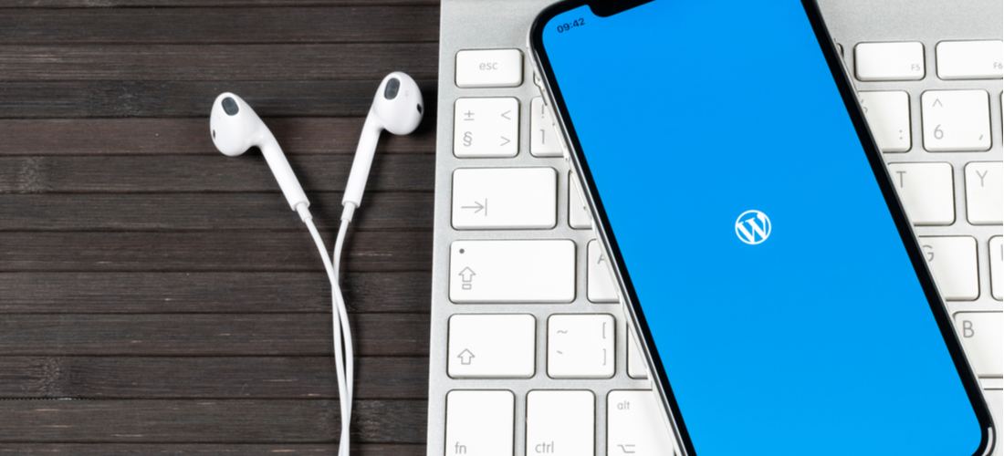 Picture of an Apple keyboard with headphone and a phone with WordPress logo pulled up