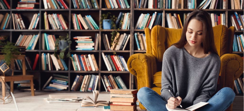 Woman writing in notebook sitting in front of bookcase