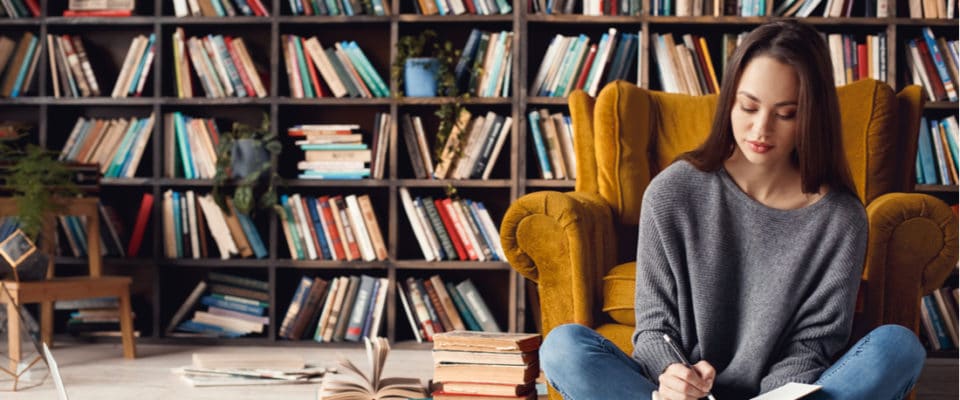 Woman writing in notebook sitting in front of bookcase