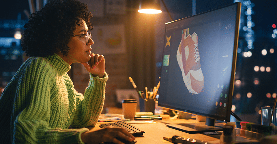 a woman wearing glasses and a green sweater reviews a 3D model of a shoe for use on an eCommerce website