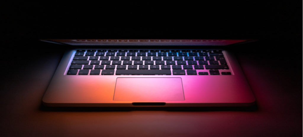 Image of Mac laptop in dark mode on desk with colorful light shining on keyboard. WordPress dark mode