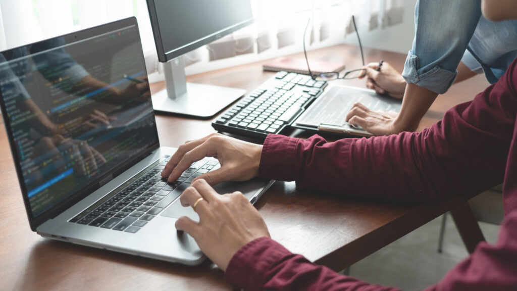 The hands of two developers in front of their laptop and screen as they build a website.